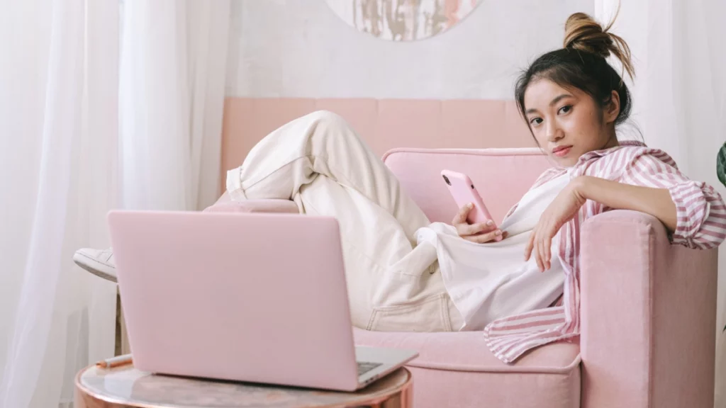Mulher usando notebook e celular em ambiente aconchegante, representando a transição de carreira para o mercado de games e tecnologia.