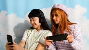 Mulheres gamers utilizam smartphone e console portátil enquanto compartilham experiência de jogo, ilustrando a evolução no competitivo de VALORANT.