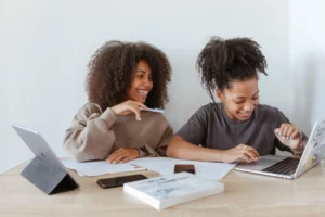 Duas mulheres utilizando notebook para pesquisar e ajustar configurações de desempenho, analisando opções que podem melhorar a experiência em jogos competitivos como Valorant